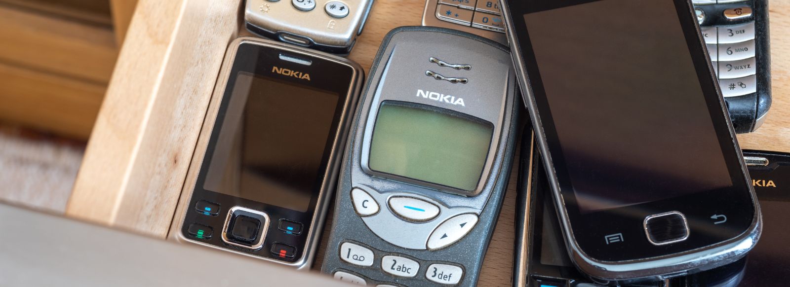 Een opengeslagen houten lade vol met diverse oude mobiele telefoons en smartphones, als symbool voor het telefoonverbod op school.