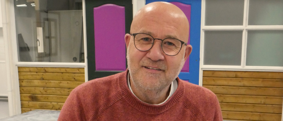 Portretfoto van Chris met een bril en rode trui, zittend in een praktijklokaal, ter illustratie van de overstap van zzp naar loondienst.